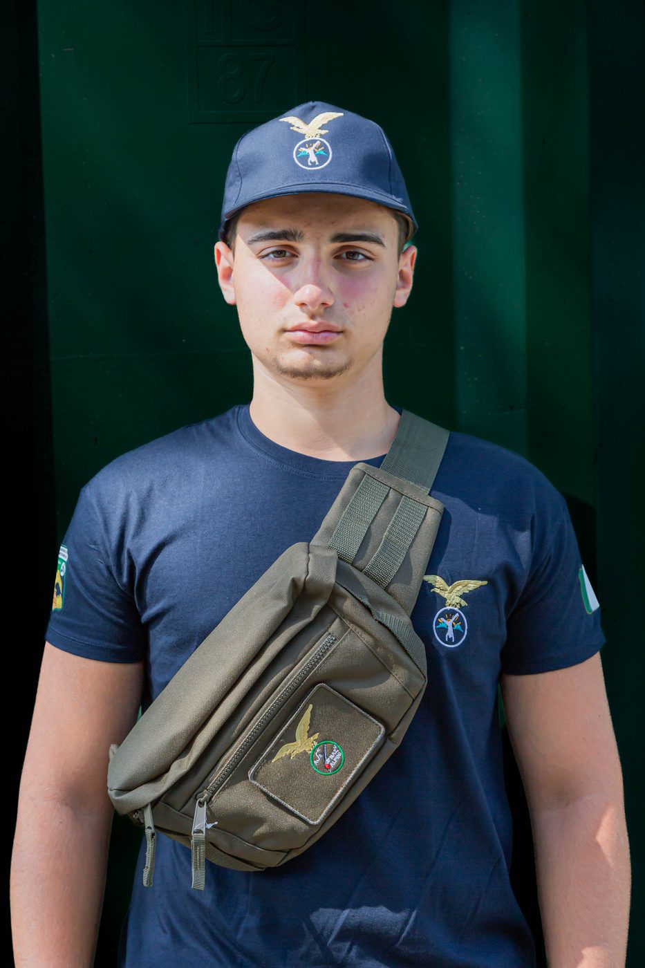 Marsupio verde con logo ricamato, portato a tracolla sopra la maglietta blu