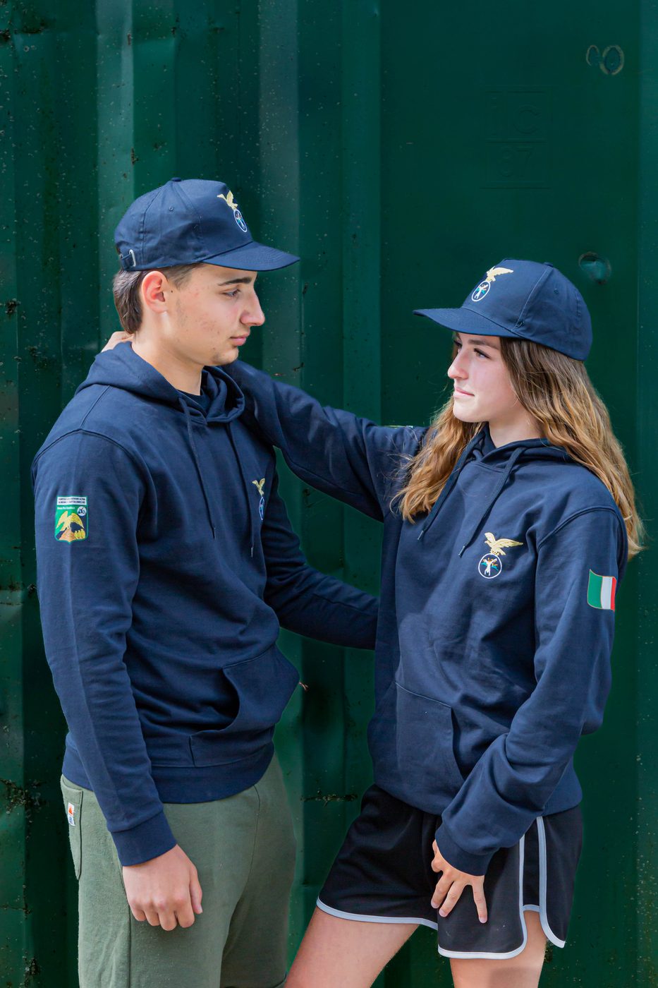 Coppia di ragazzi con felpa blu con cappuccio davanti al container del campo
