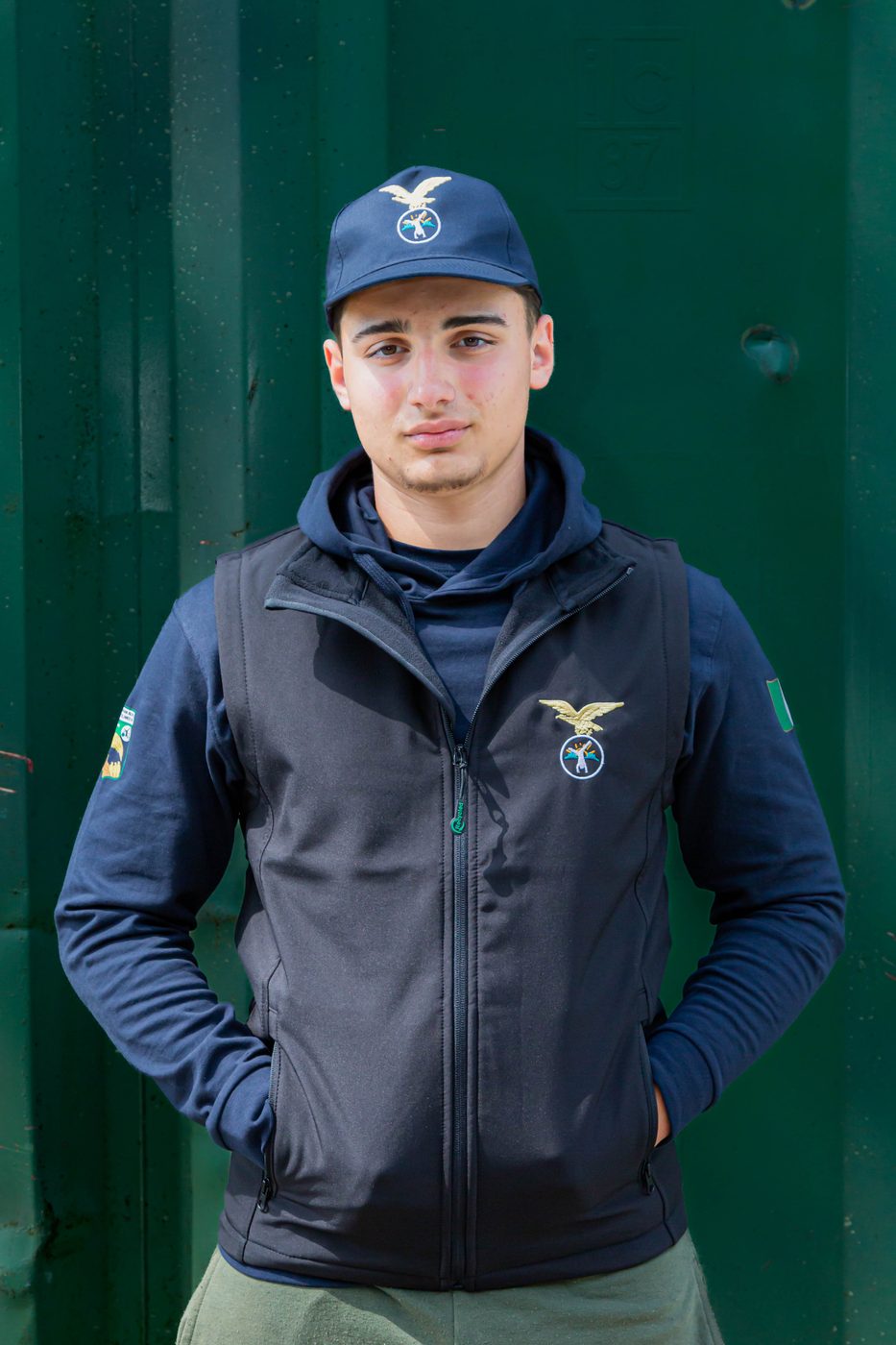 Ragazzo con gilet smanicato nero indossato sopra la felpa blu, con cappellino blu