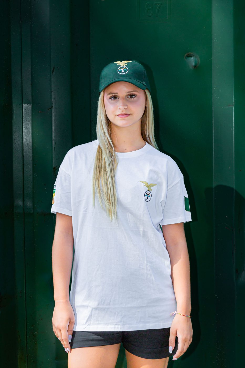 Ragazza di fronte con maglietta bianca del Campo Scuola e cappellino verde